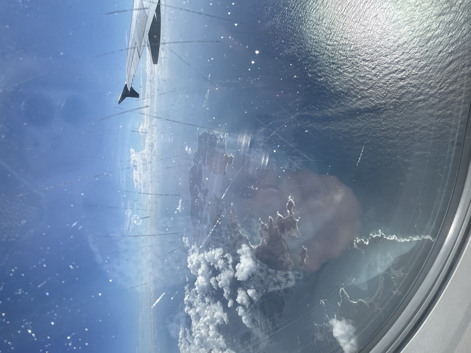 離陸直後の機内の窓から見た翼と、はるか下の雲