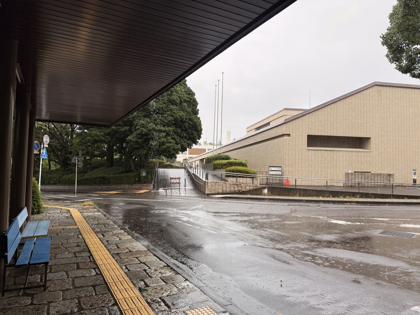 雨にぬれた静岡県立美術館の入口前の道、屋根の下にベンチと点字ブロック