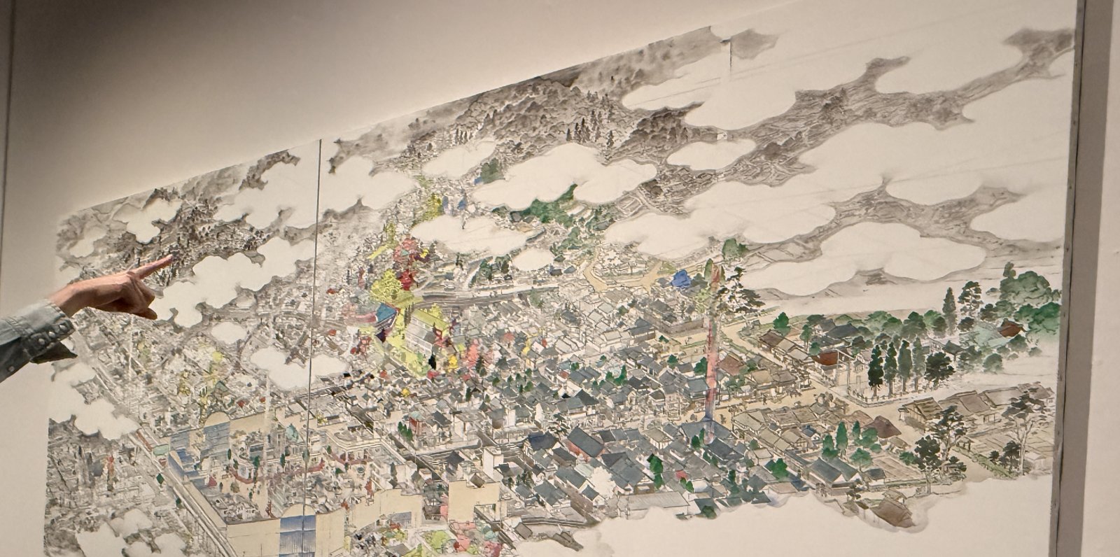 雲のあいだに町並みがびっしり描き込まれた山口晃の大きな鳥瞰図を、指さす手