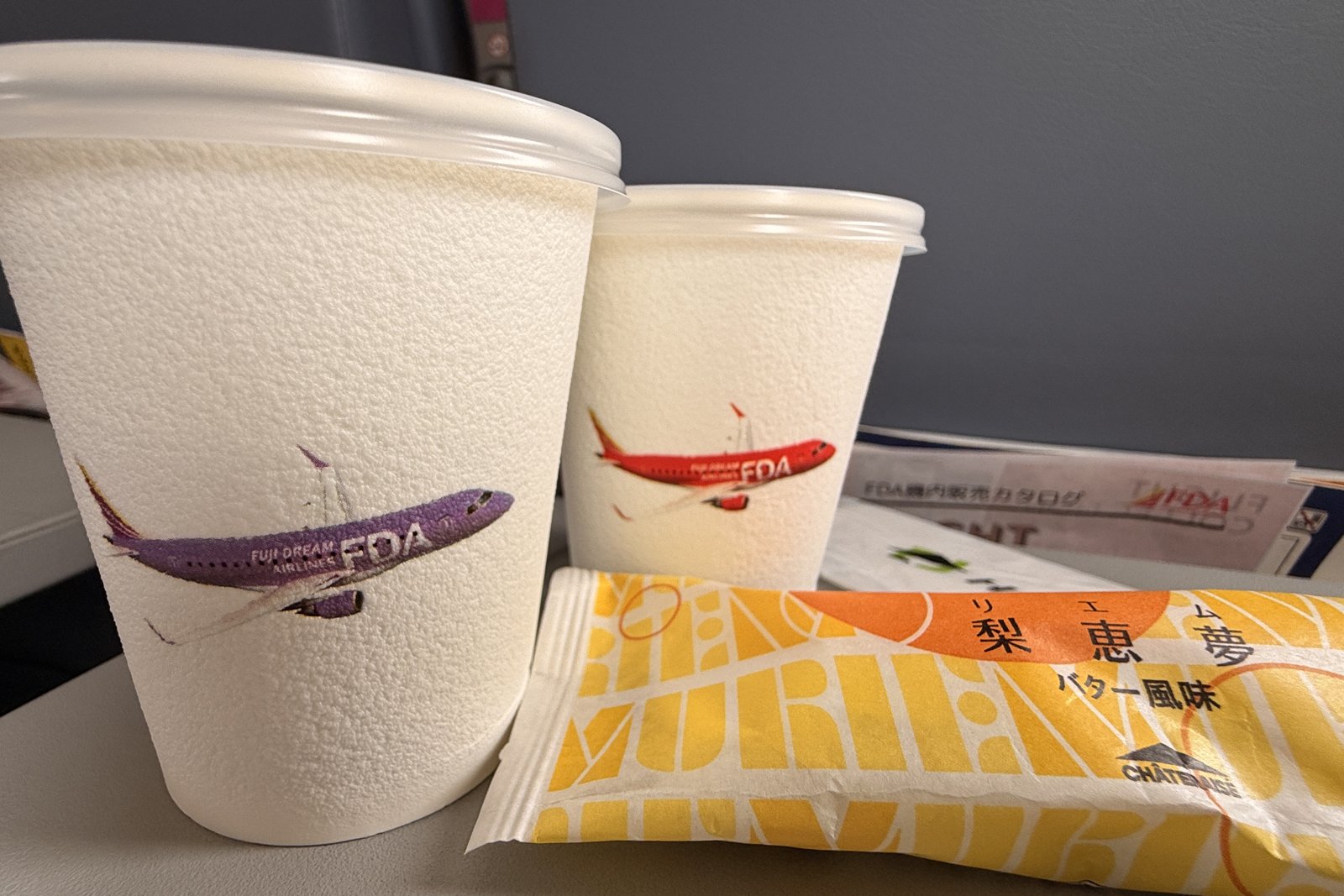 FDAの機内サービス、飛行機の絵がついた紙コップとシャトレーゼのお菓子